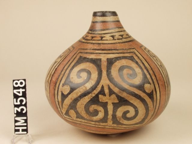 Cocle polychrome ceramic bottle. The side panels depict claws. The front and back panels use Y-elements to suggest an abstract frontal face or crested head. The face is formed by two pointy-nosed crested animals in profile, facing each other. The crest is formed by the tail-ends of the profiled creatures.