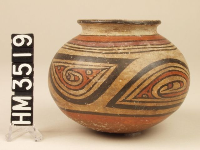 Cocle miniature polychrome ceramic jar. Pica Pica variety. A red "Y" element design inside the black border of an oval panel depicts a profiled creature with a pointed nose, a curly head crest and a horizontal eye slit. A tail end in the form of a second head is also indicated by a slit eye. A single basic "Y" element forms the overall body, and the tail (head) end and crested head end are crested by additional "Y" elements. The entire design may represent a life form, possibly embryonic, inside a boa oval.