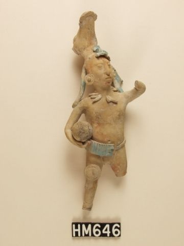 Small ceramic figure holding ball and wearing elaborate headdress. Elements of outfit are picked out in blue.