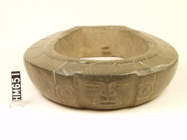 Carved stone object, an elongated ring shape with a face incised in the front.