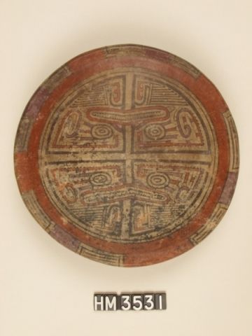 Polychrome ceramic plate. A central band of boa kennings divides plate into two hemispheres. Each hemisphere is further divided into halves that are conjoined by features of a frontal face and clawed limbs of an iguana-boa. The clawed limbs are colored in one hemisphere but not in the other, which suggests an incomplete design. Furthermore the head crest in one hemisphere is curled at the tip while the one in other hemisphere is more pointed. This type of asymmetry may indicate female versus male.