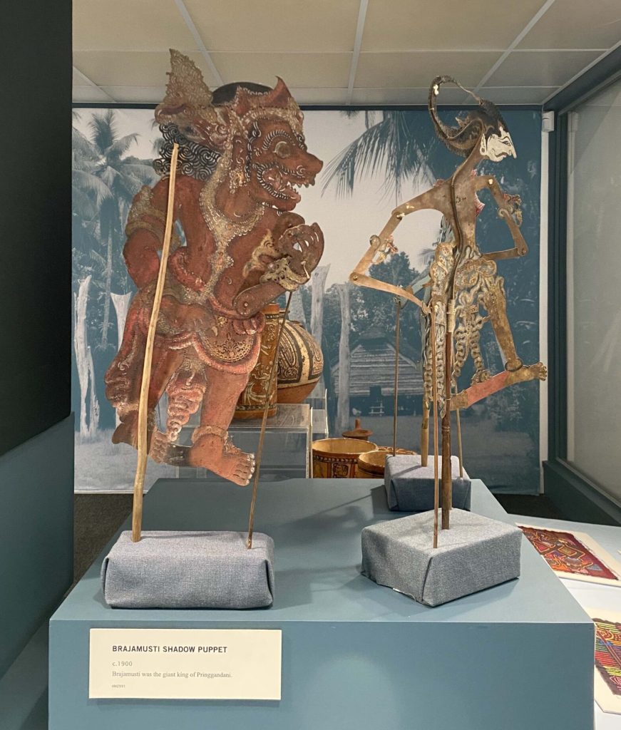 Two shadow puppets on exhibit. One is reddish-brown and stout, the other is thing with a pointed white face.