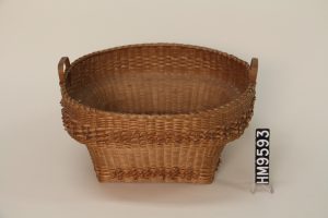 Image of a woven basket with a square bottom and round top. The basket is woven in such a way that the opening at the top is significantly wider than the base.