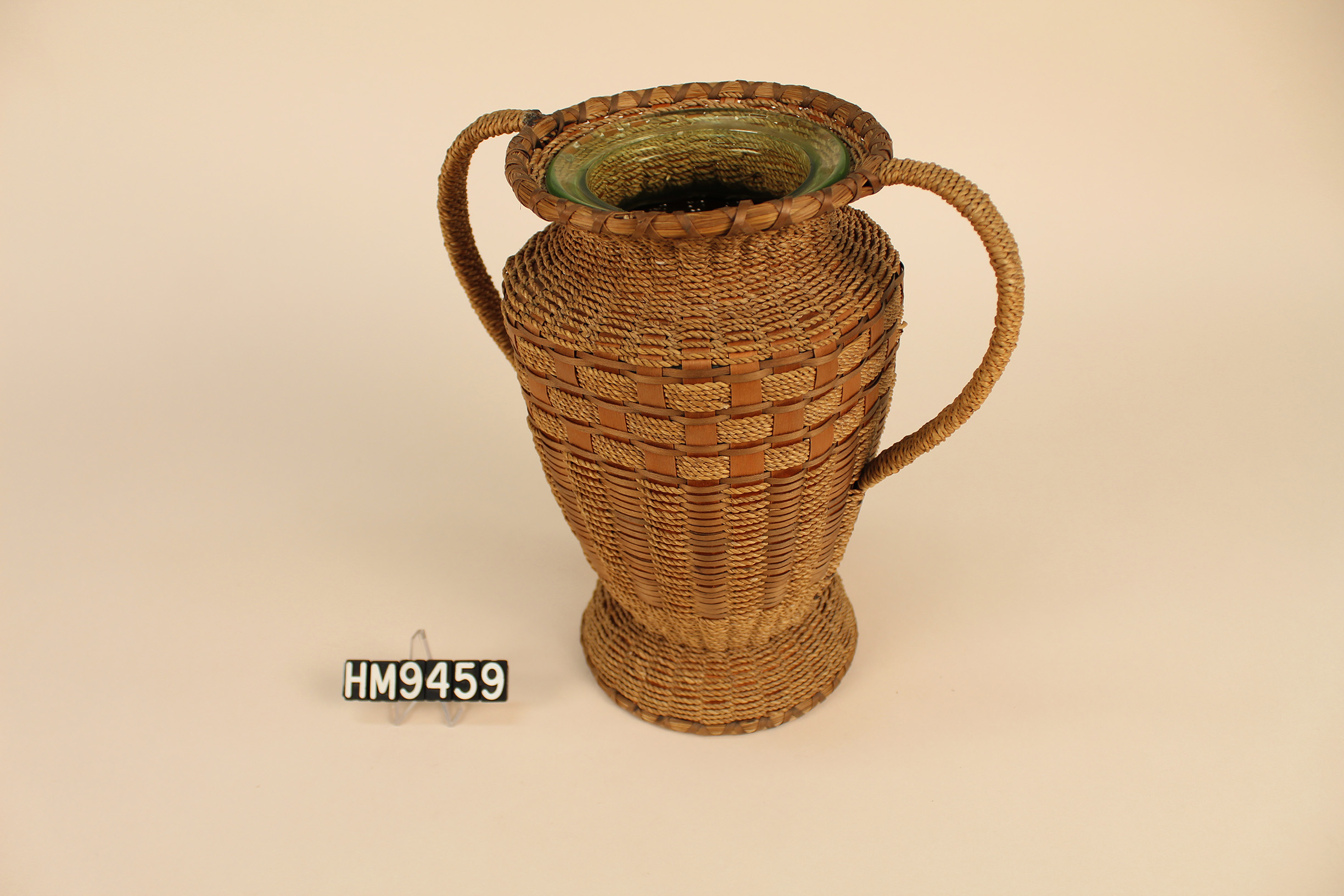 Basket woven around glass vase with handles giving it the shape of a classic trophy.