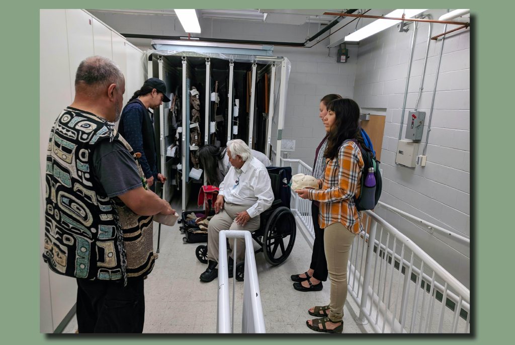 Color image of an access ramp in the interior of the Hudson Museum. A group of Tlingit representatives are shown examining textile artifacts.