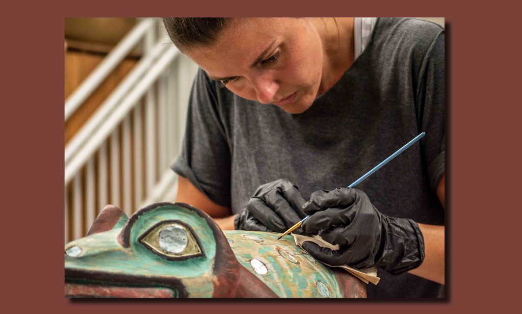 Image of Anna Martin painting final details of the replica on abalone.