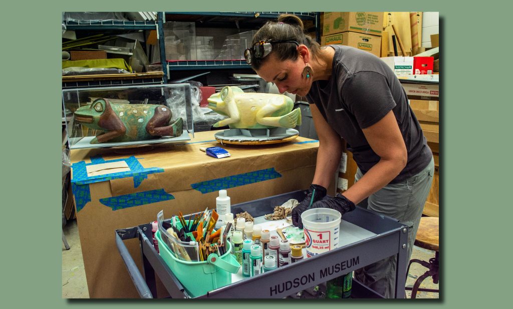 Image of Anna Martin preparing paints for the final coats on the replica, with the original placed next to it in a protective glass case. 