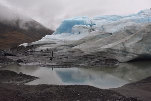 A person looking at the edge of a glacier near a small body of water