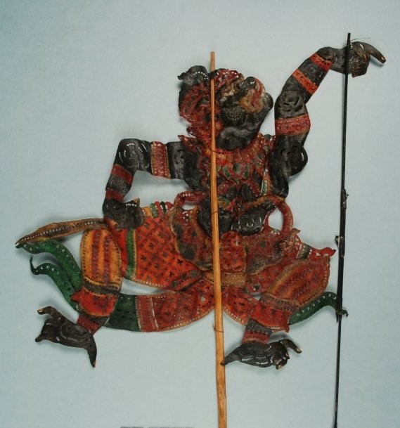 Shadow puppet of a Hindu deity with black skin and red clothing.