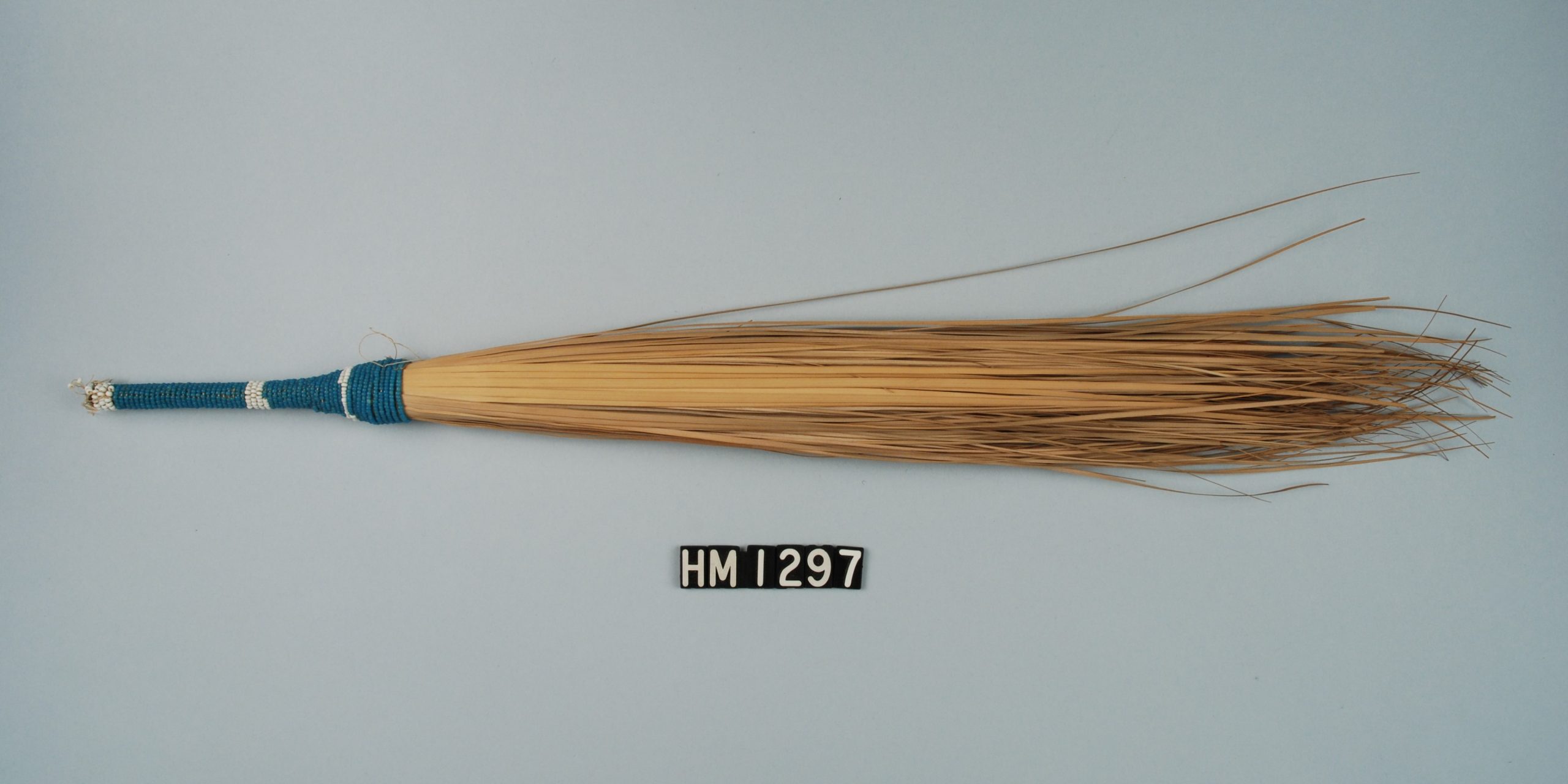 Image of a fly whisk made of long strands of grass held together at one end by a beaded handle.