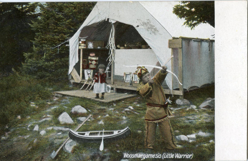 A colorized image of two children in front of a tent with spruce trees in the background. The smallest child is near the tent, the older is a little boy nearer the viewer, dressed in Native dress and aiming a small bow and arrow up into the trees. Baskets can be seen in the tent and a small toy canoe is on the ground by the boy.