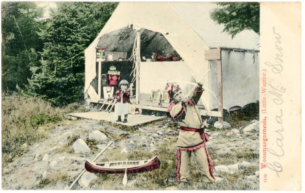 A colorized image of two children in front of a tent with spruce trees in the background. The smallest child is near the tent, the older is a little boy nearer the viewer, dressed in Native dress and aiming a small bow and arrow up into the trees. Baskets can be seen in the tent and a small toy canoe is on the ground by the boy.