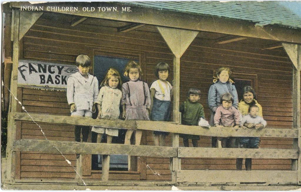 A colorized image of nine children of various ages standing on a porch. The sign behind them reads "Fancy Baskets"