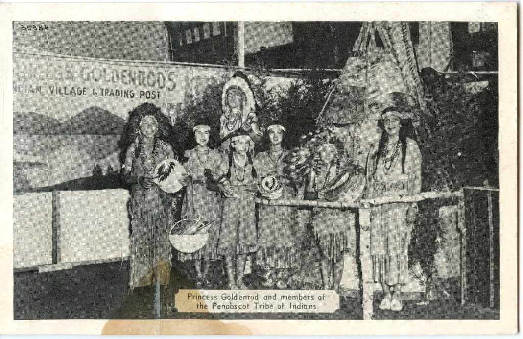 A grayscale image of a family in Plains-style Native dress standing in front of a small, birchbark-covered tepee and a sign that reads "Princess Goldenrod's Indian Village & Trading Post"