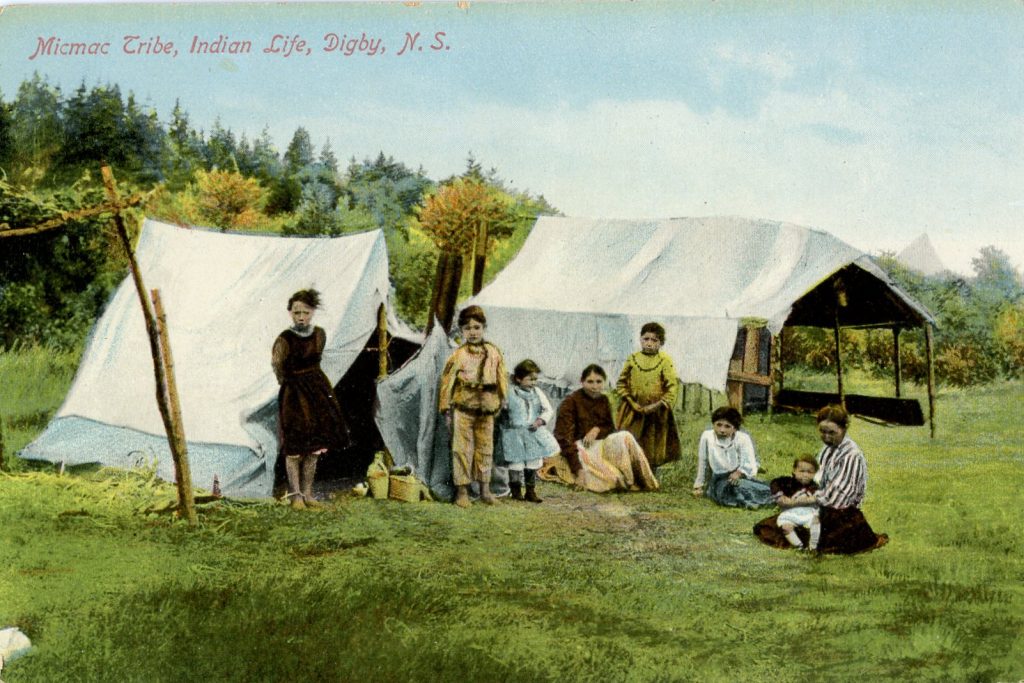 Colorized image of two women and six children in mostly European-style dress gathered near two canvas tents. A few baskets can be seen hear one of the tents.