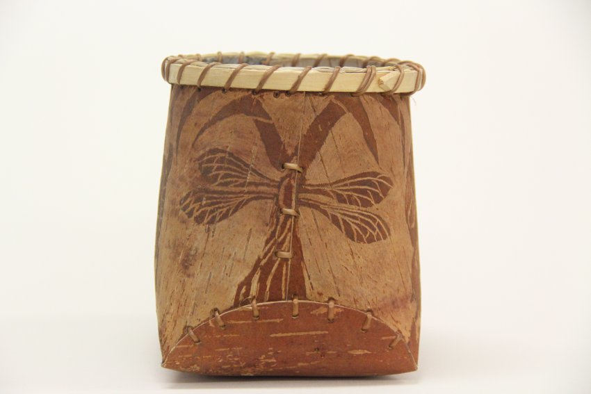 Image of a small birchbark container. The side has been etched leaving the image of a dragonfly set against a light background.