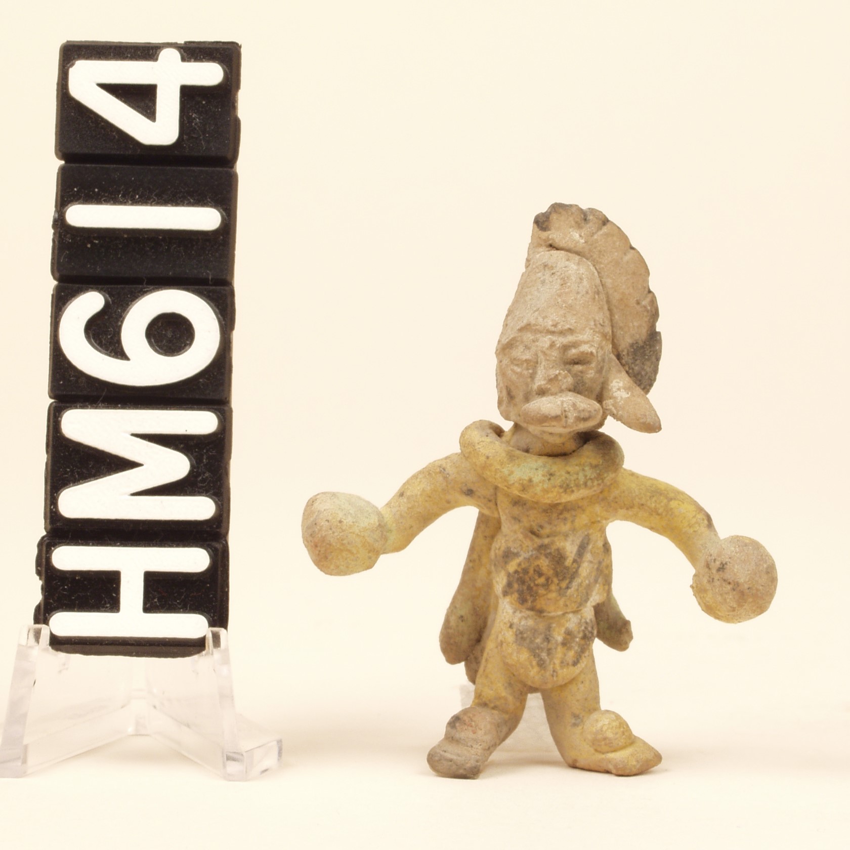 Image of a tiny ceramic figurine of a humanoid with a headdress and little balls on the hands.