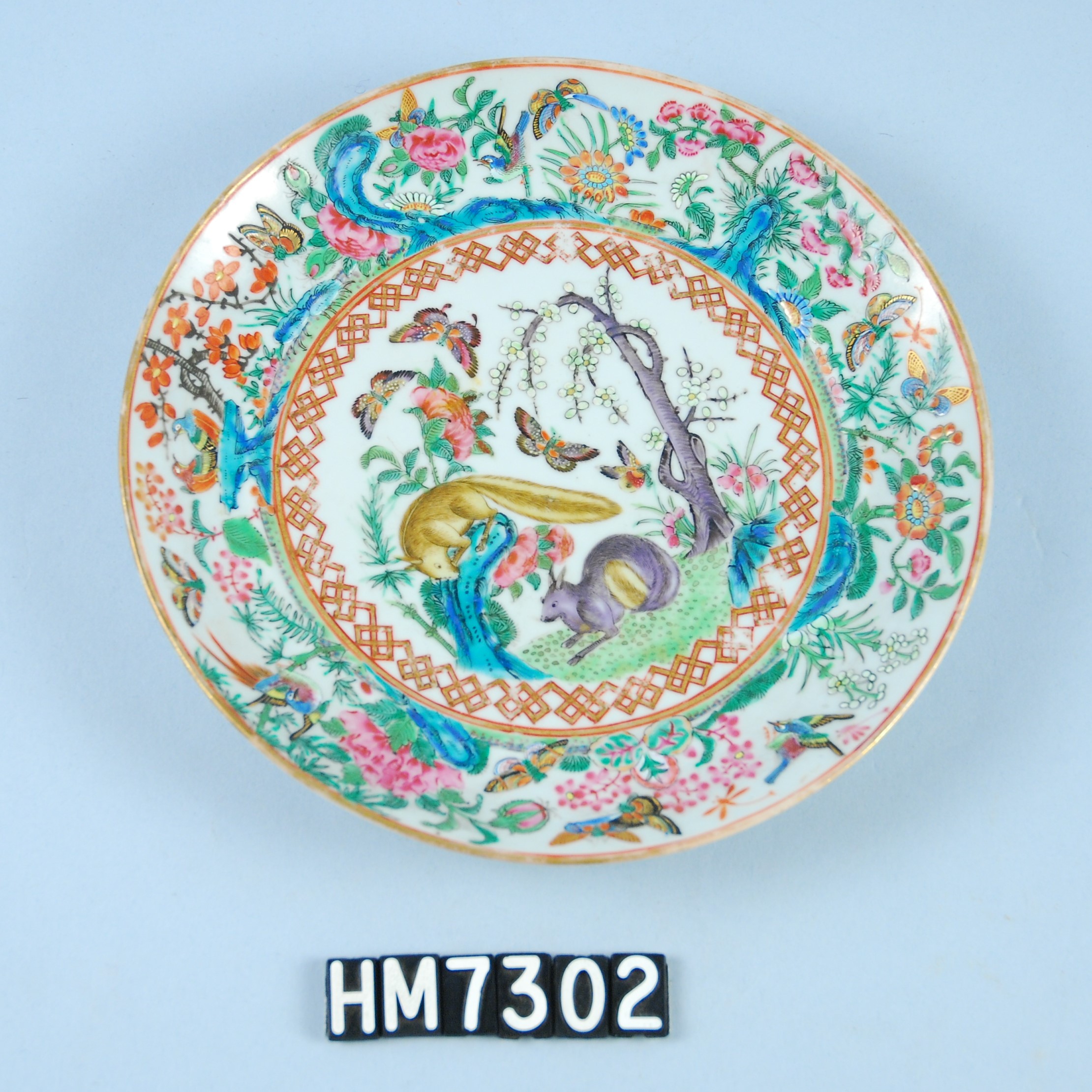 Image of a colorful porcelain plate featuring a wide array of plants and animals, including butterflies and birds.