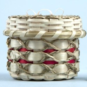 A small, decorative basket with wide weavers, braided sweetgrass decorations, and red details.