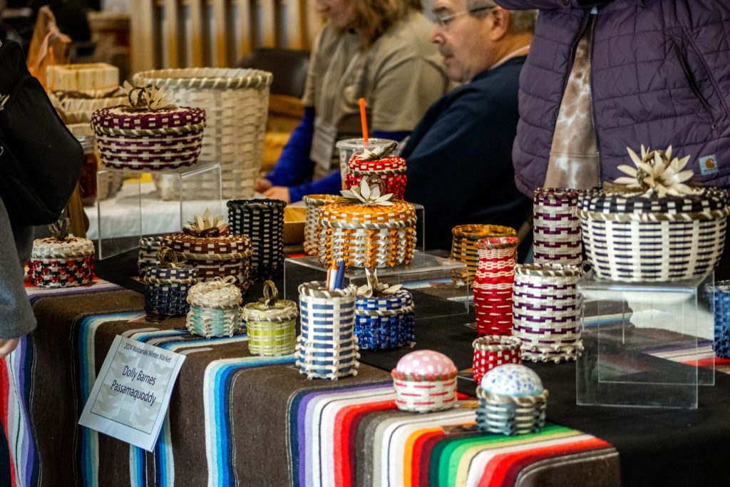 Photograph of colorful baskets displayed on a table covered in a striped cloth.