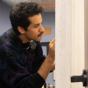 A man with a mustache and headphones around his neck focuses intently on an artwork we cannot see.