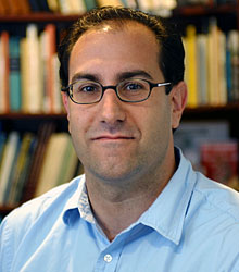 Image of Penobscot man wearing glasses and smiling slightly with a bookshelf in the background.