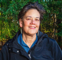Image of Penobscot woman with short, dark hair, smiling with a tree in the background.