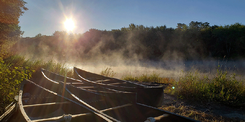 Image of canoes with fog rising off lake in background.