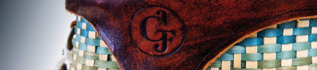 Detail image of a leather cover on a colorful basket. Cover is stamped "GF"