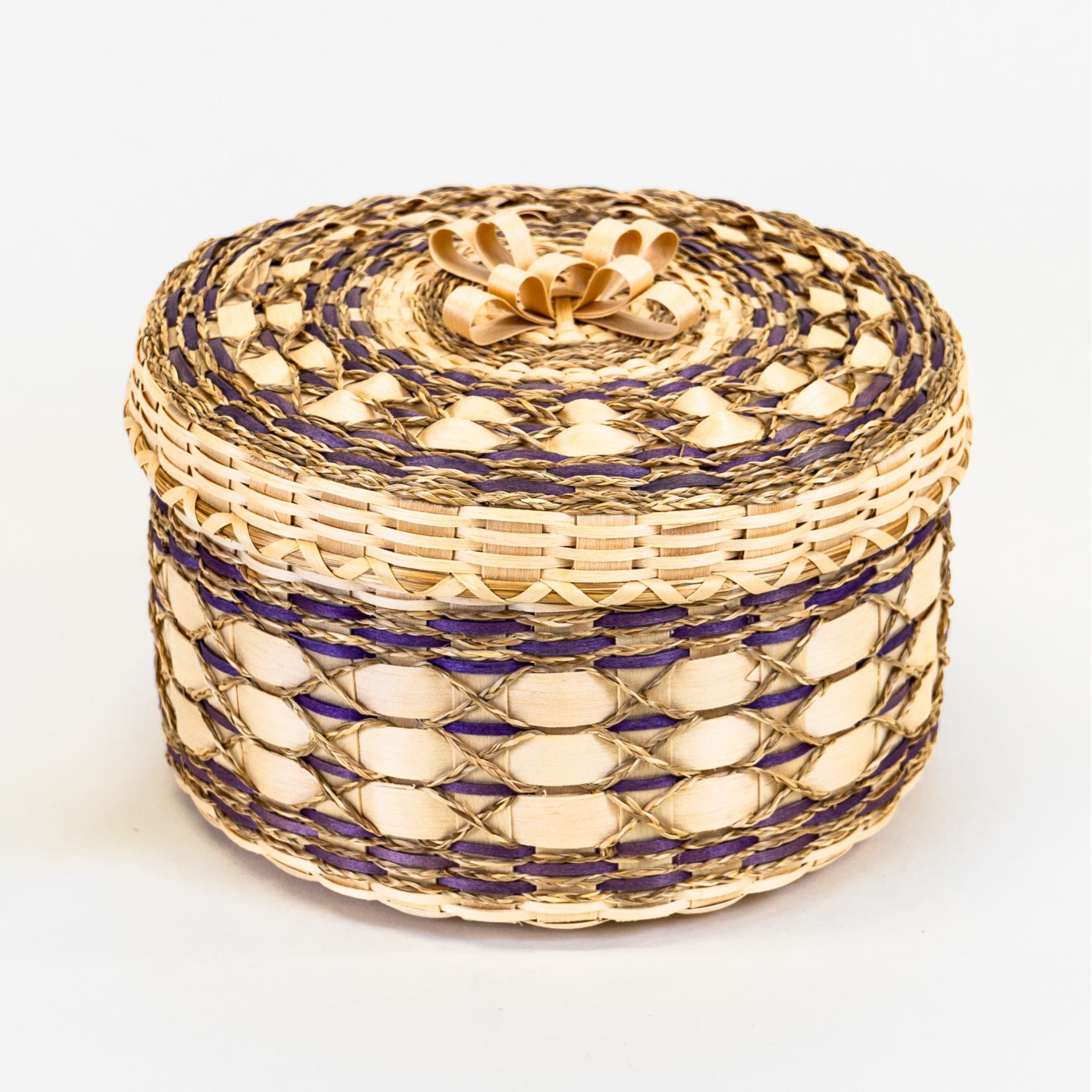Image of intricate basket with fine braided sweetgrass, purple details, and a decorative brown ash bow on the cover.