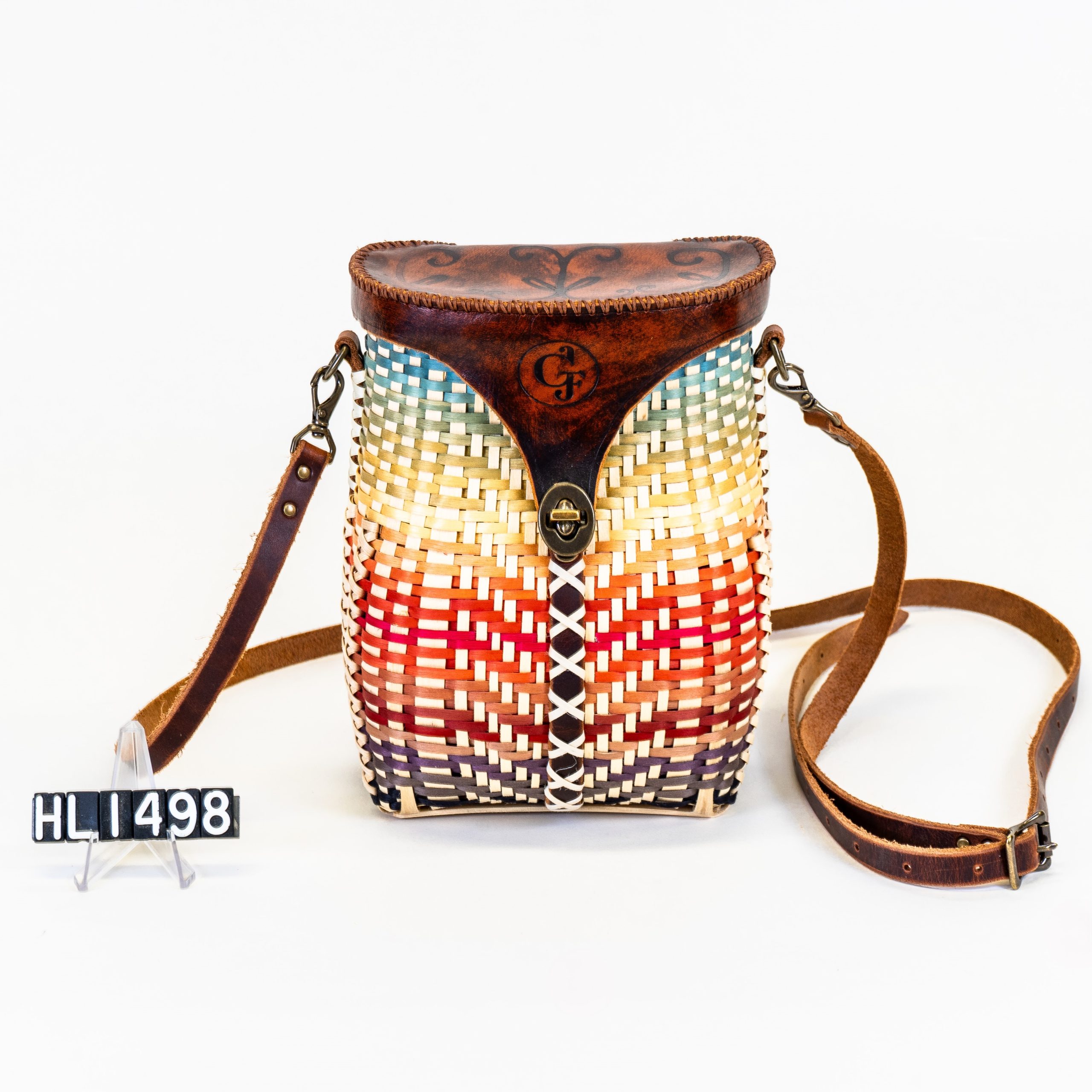 Image of basket in shape of pack with leather strap and cover and with colors organized like sunset over water.