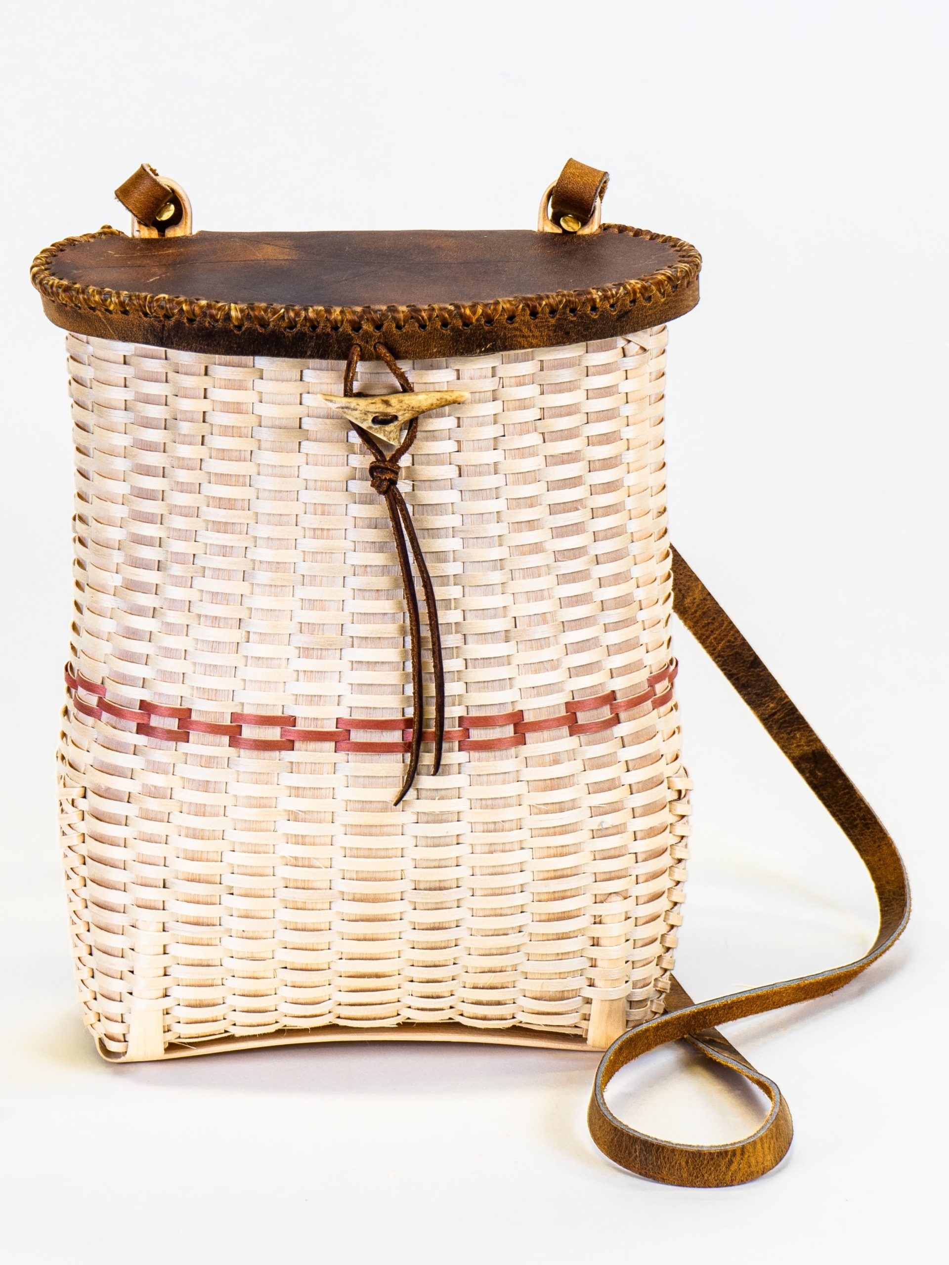 Image of basket in form of pack with leather strap and cover and with red stripe.