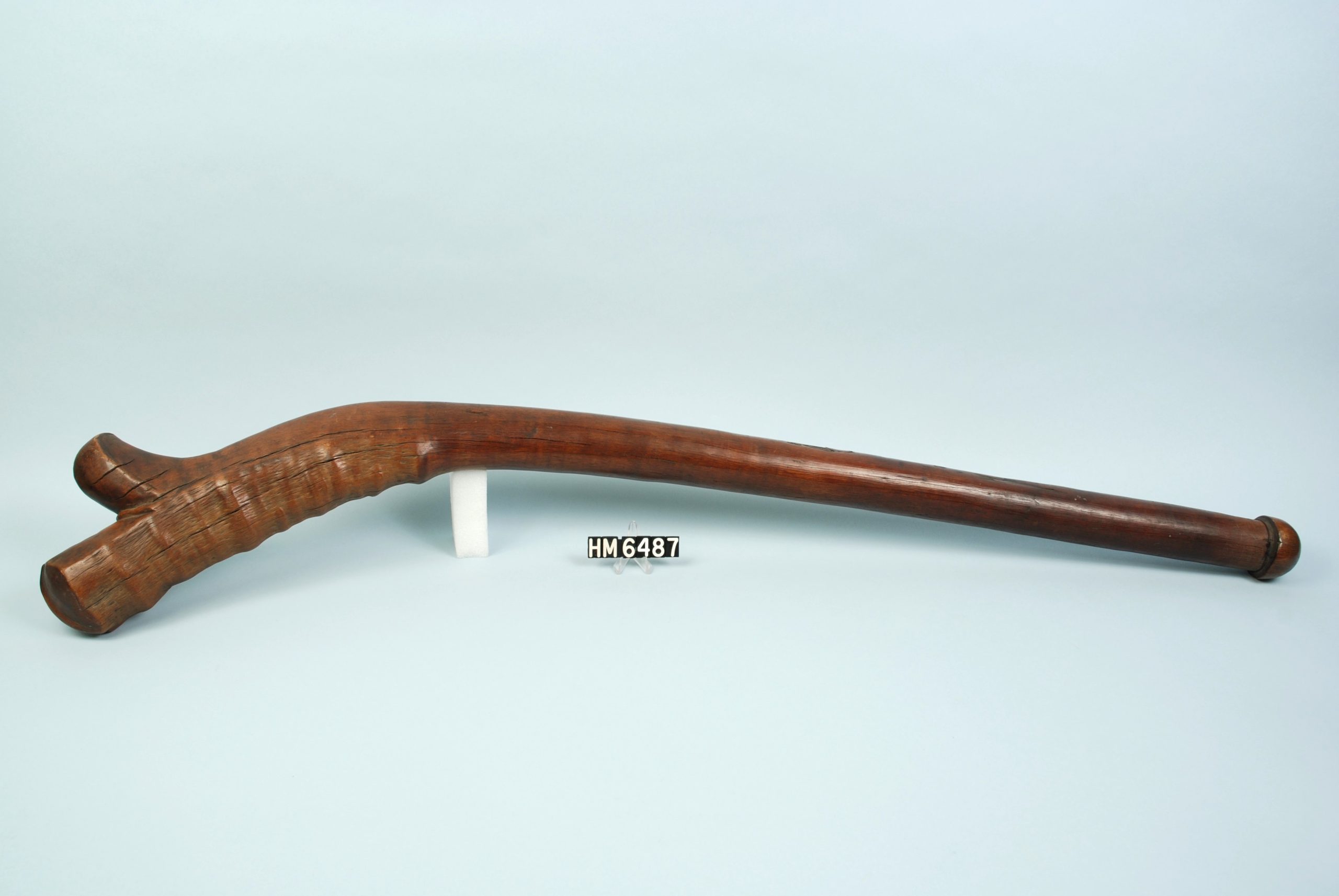 Image of a long club formed from a single branch, curved at one end with a small knob protruding.