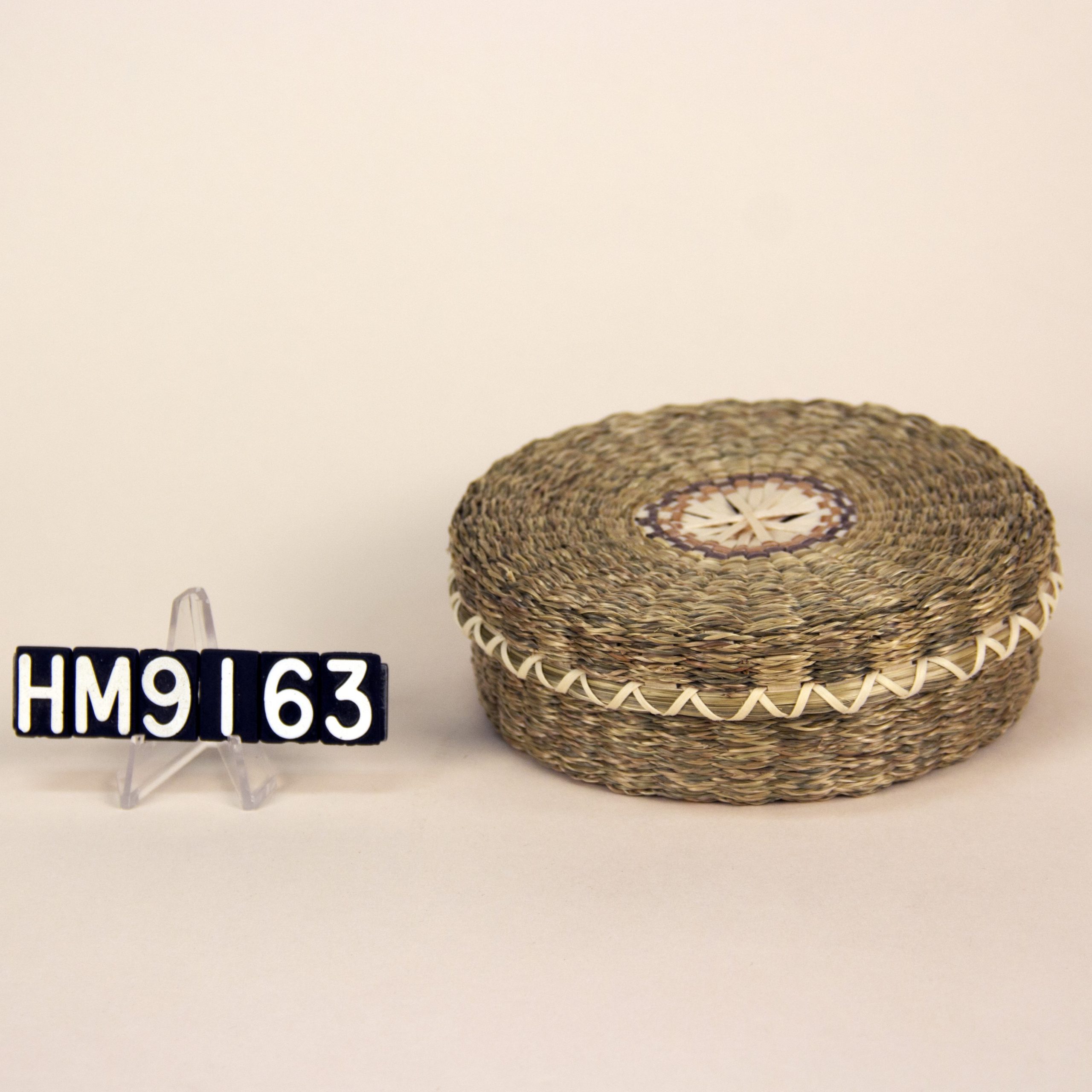 Image of small, round basket with muted colors and sweetgrass braids.