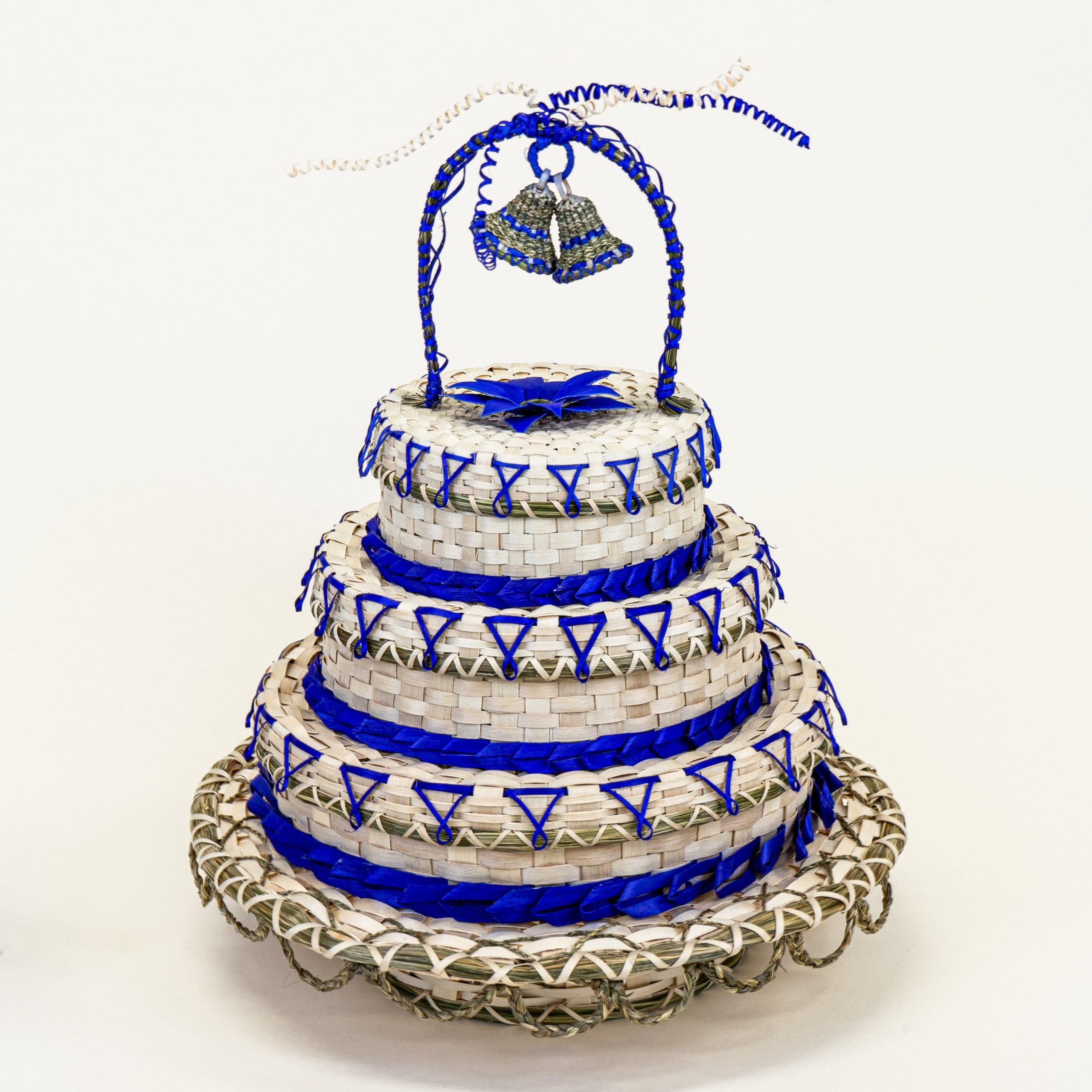 Image of a basket shaped like a three-tier wedding cake on a stand. Heavily decorated with bright violet weavers and braided sweetgrass and topped with an arch with two basket bells and sweetgrass curls.