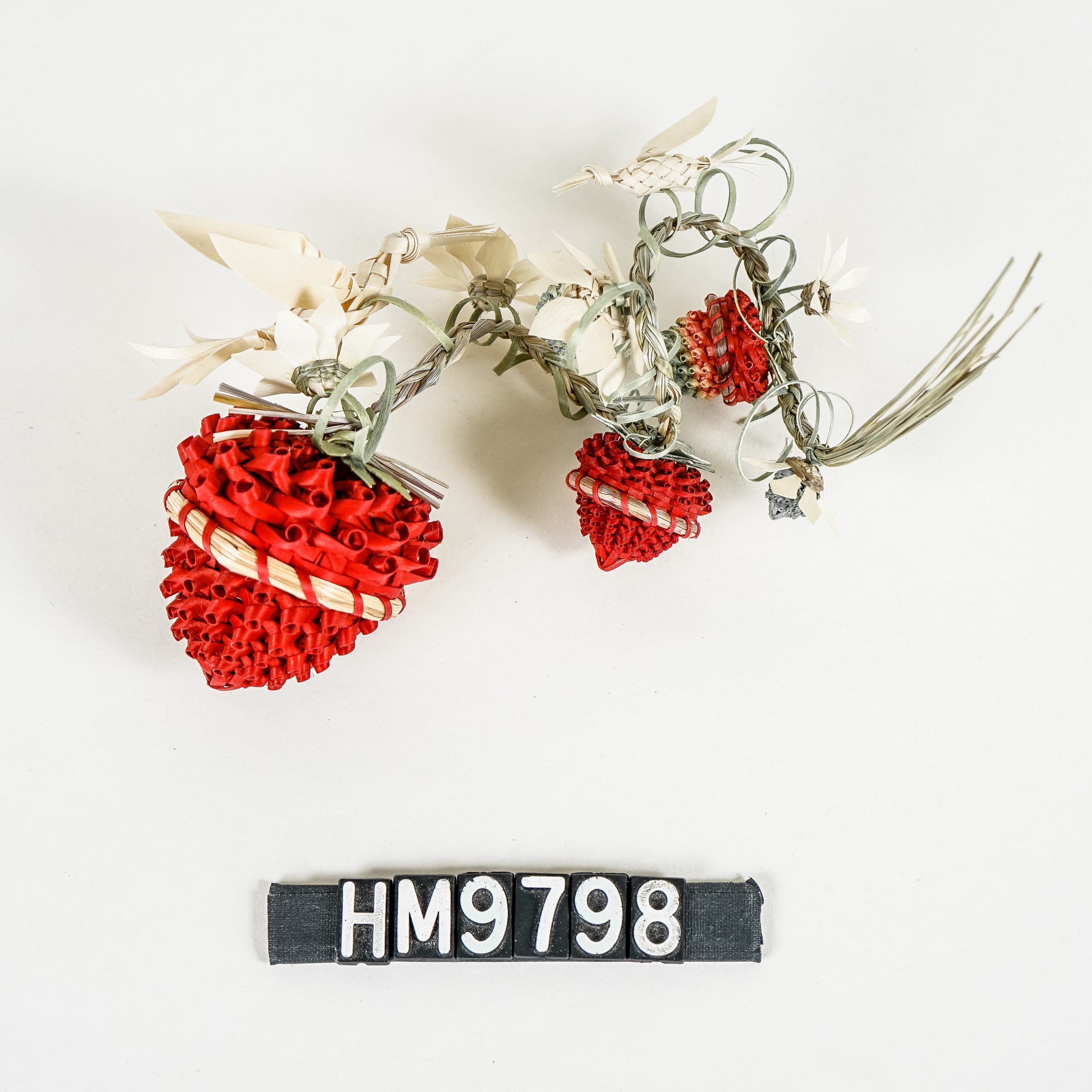 Image of baskets shaped like strawberries of decreasing sizes and two brown ash birds strung on a curled braid of sweetgrass.
