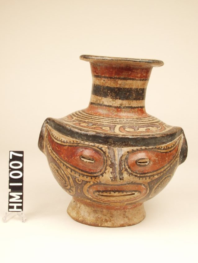 Polychrome ceramic effigy jar in the form of an effigy head with red painted mask around eyes, tall spout with red and black rings.