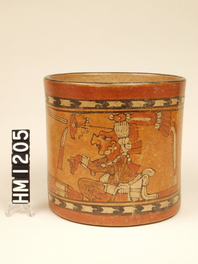 Wide ceramic vase with vertical sides. Black and white chevron bands approximately 3/4 inch from base and rim. Between is a seated figure dressed in a white loincloth and elaborate headdress facing left with right arm extended and palm in downward position.