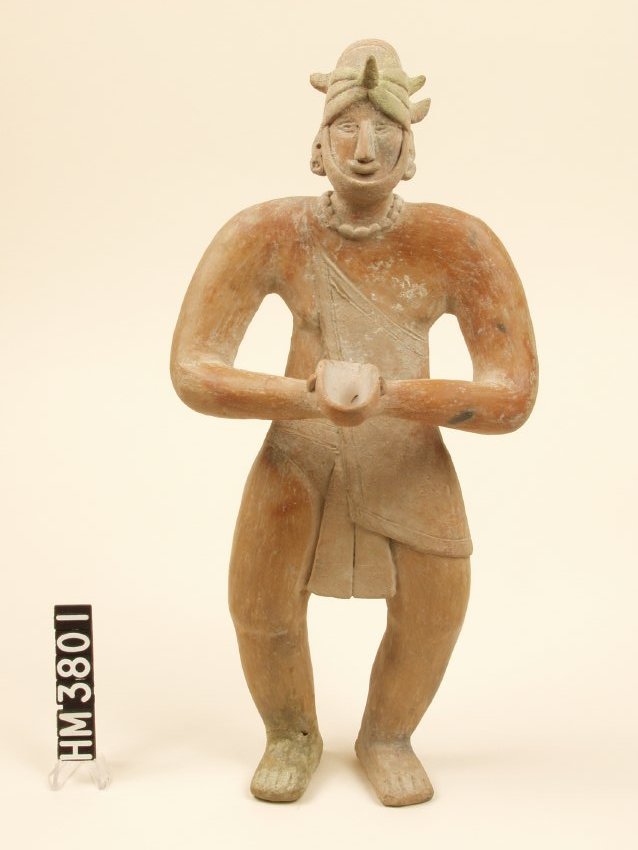 Standing ceramic figure holding offering bowl. Legs slightly bent. Wearing cloth wrapped around body and draped over one shoulder, an elaborate headdress, a necklace, and ear spools.