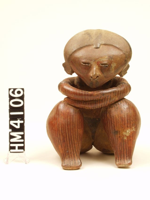 Ceramic figure seated with her arms drawn up to chest. Exaggerated bulbous legs and hips, flattened stylized feet. Long ropy, folded, arms that rest on knees. Thin, narrow eyes and mouth, and a large pierced nose. Vertical lines have been painted on legs, arms, and back. 