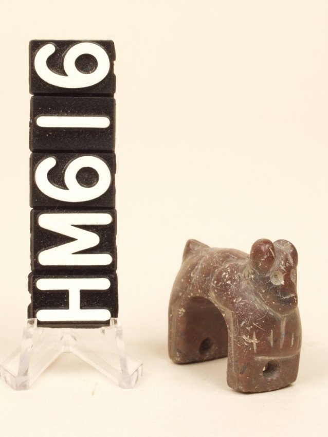 A small carved stone object in the form of a half of a ring, shaped like a small animal, with a hole at each end.