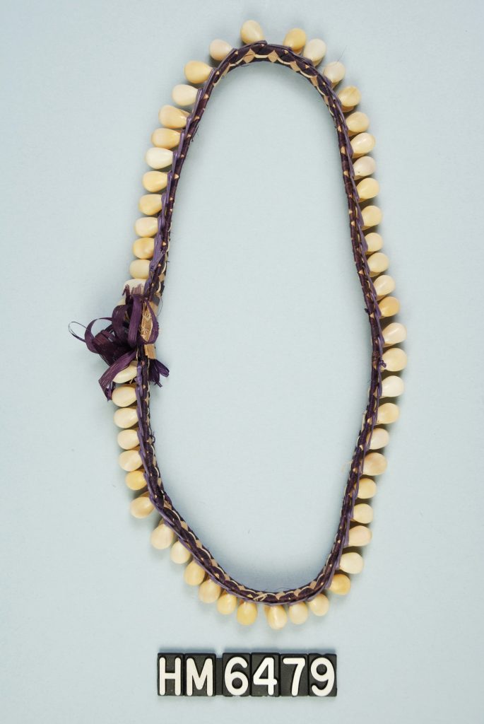 Image of ornament made with shells attached to woven band with bow.