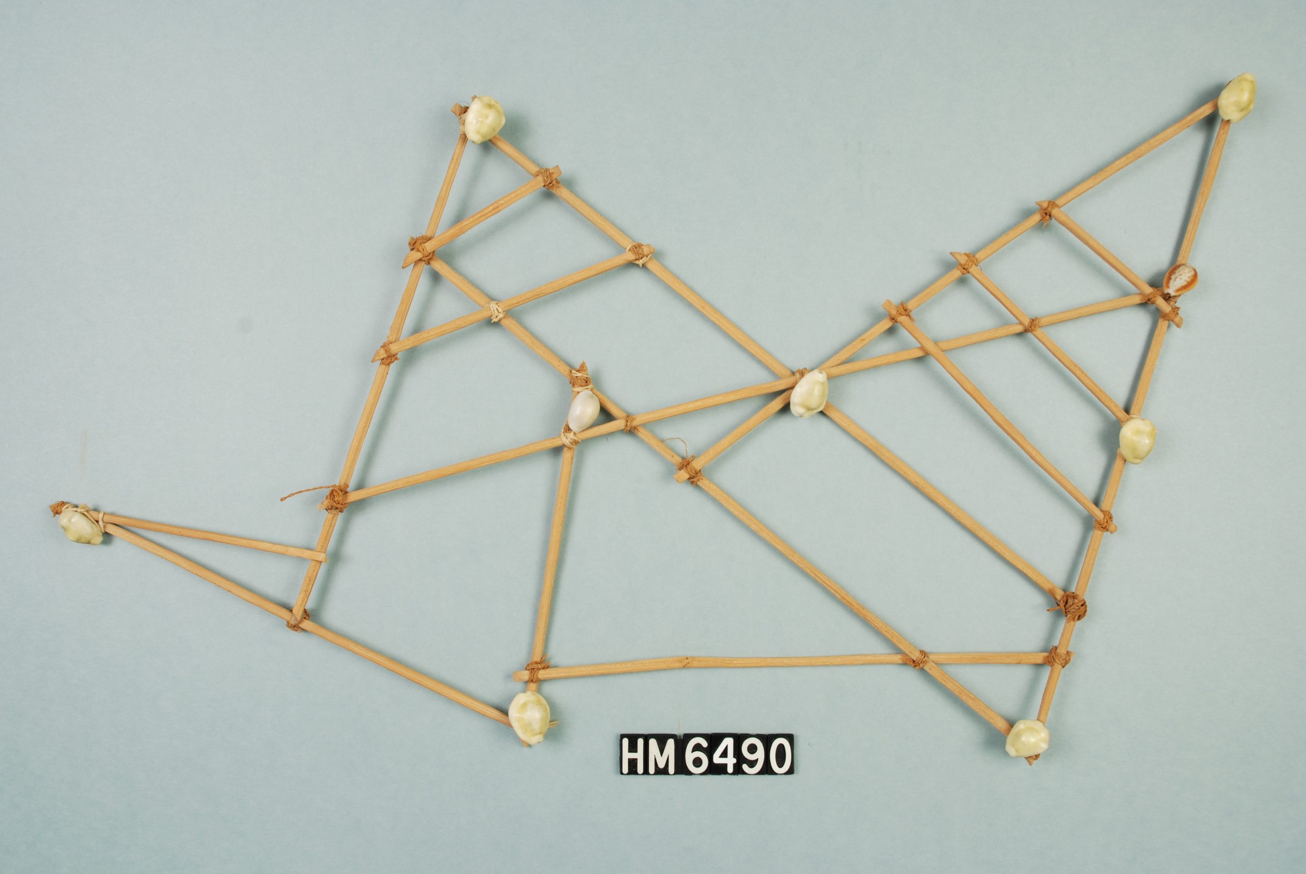 Image of a object consisting of sticks lashed together forming angular patterns.  Shells are attached at some of the joins.
