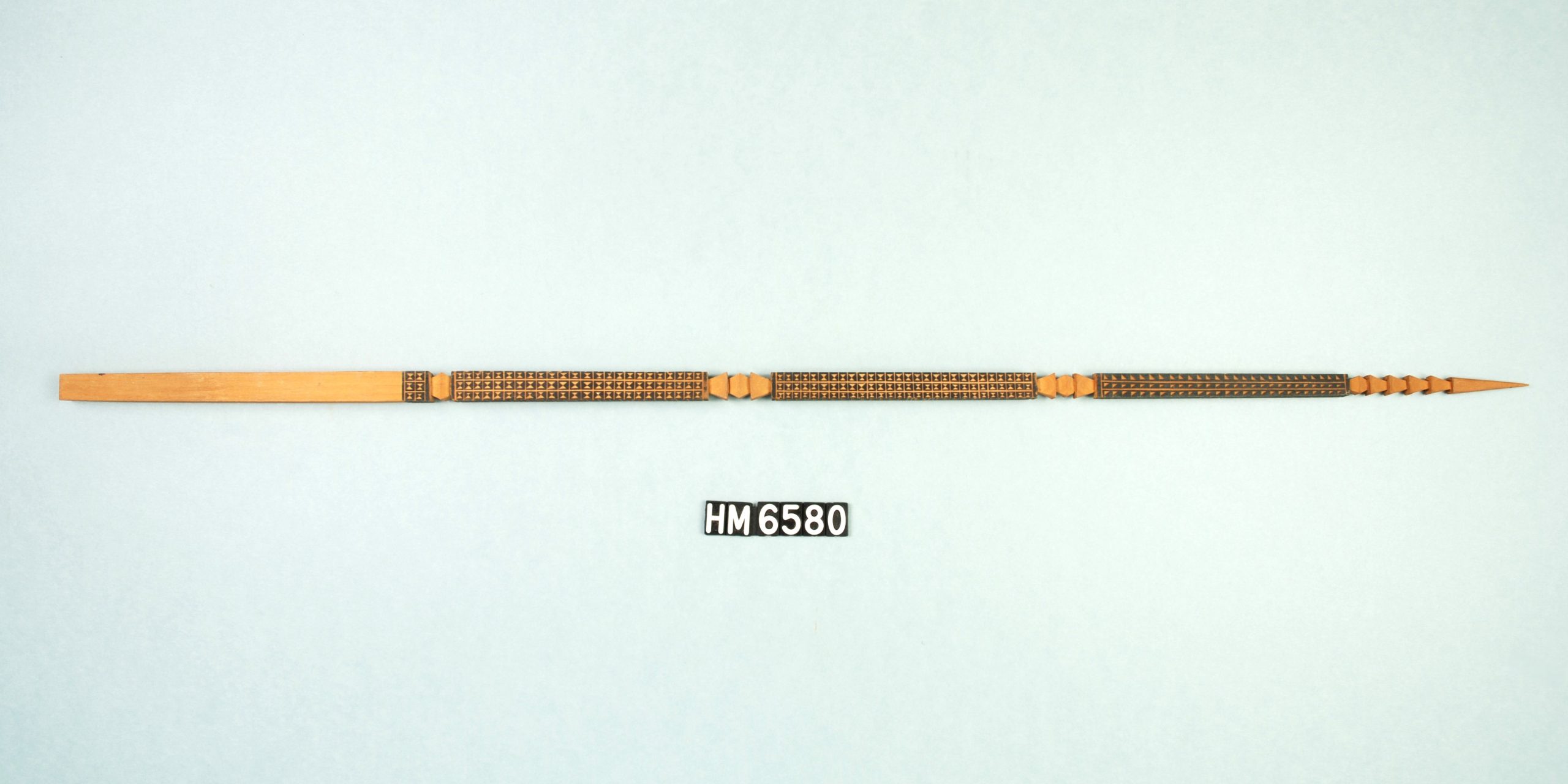 Image of stick, squared at the left end and pointed at the right. The center is decorated with carving and black and red paint.