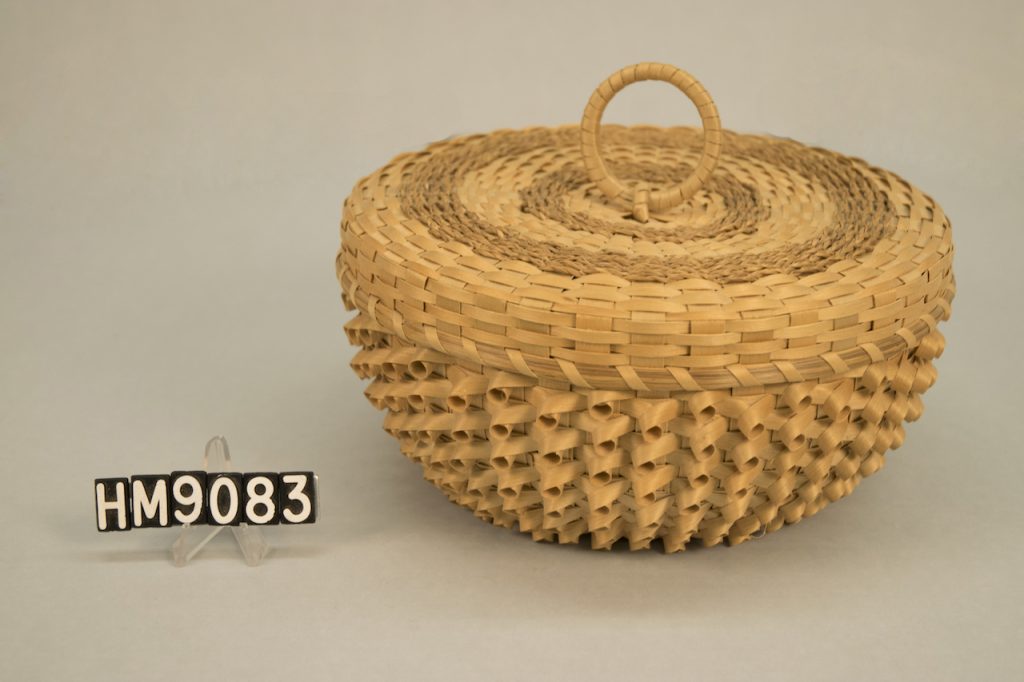 Image of wide, round basket with curl details and ring handle on cover.