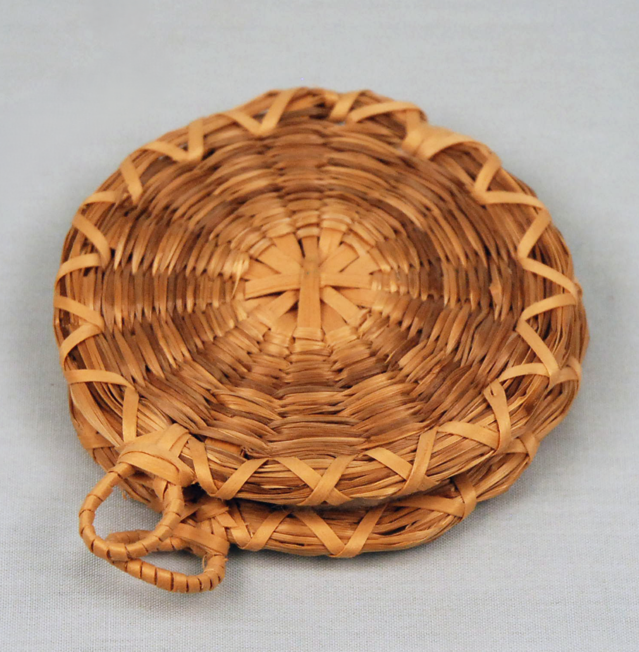 Image of small, flat, circular basket woven with single strands of sweetgrass.
