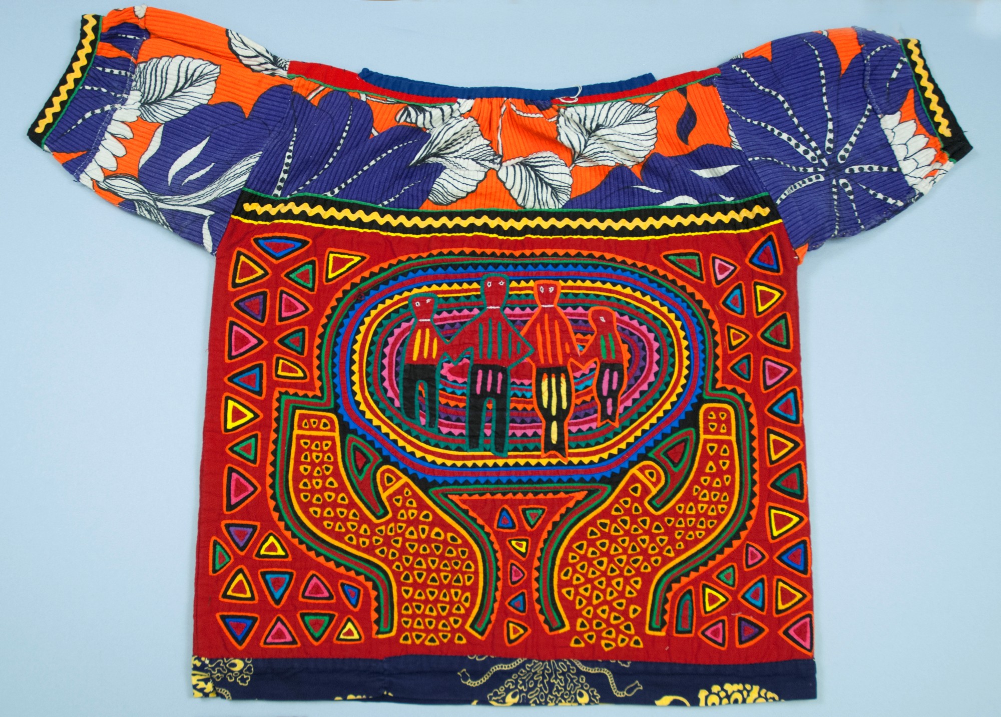 A shirt with a mola as the body and a bright floral forming the yoke and short sleeves. The mola depicts two hands holding up an oval shape containing four figures.