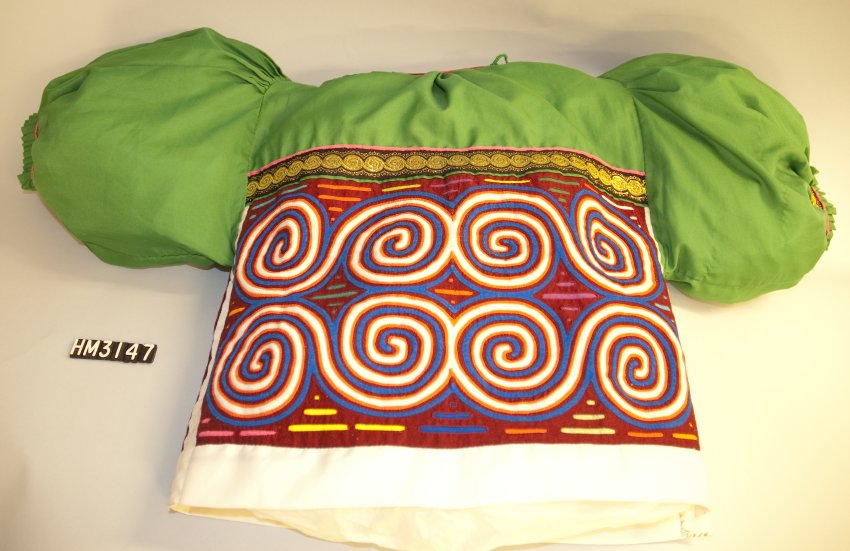 A shirt with short, puffed, green sleeves and green yoke and a mola with spiral motifs serving as the body of the garment.