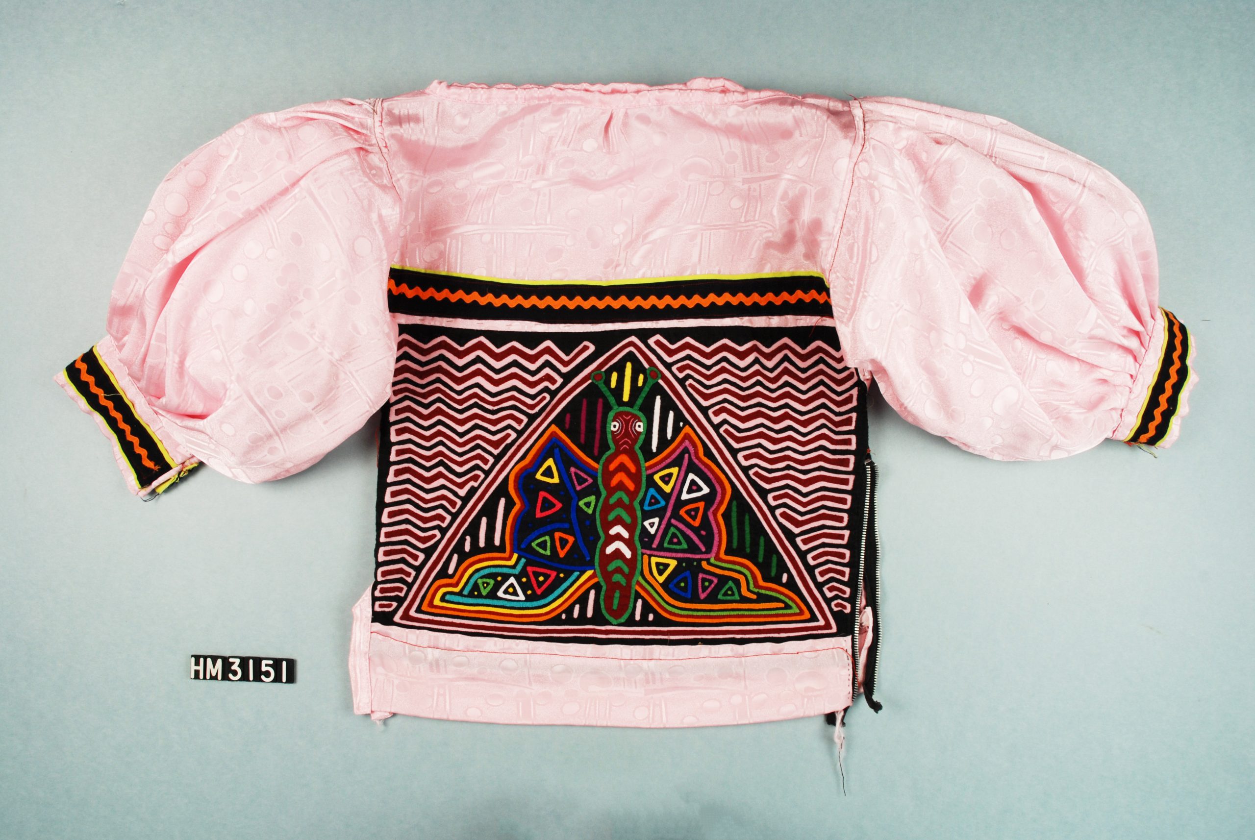 Shirt with mola serving as body of garment and shiny, pale pink fabric as the yoke and short, puffy sleeves.