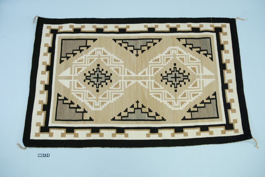 A large textile in black, cream, tan, and gray. A double-diamond motif within a multi-layered frame of patterns. Designs are intricate.